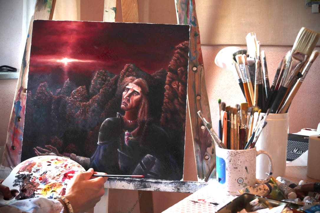 Painting on the easel in the studio: a young man in armour looks upward at a dark red sky with a bright star, surrounded by dark rock forms.