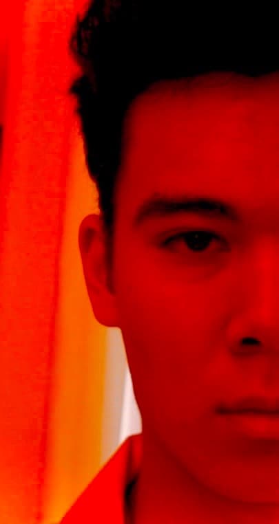 Close-up of Isak's face in strong red light. Only one half of the face is visible, and an orange surface glows behind him.